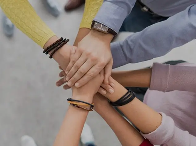 A group of people place their hands on top of each other in a gesture of teamwork and unity.