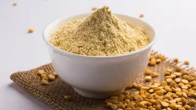A bowl filled with gram flour (besan) kept on a jute tapestry with scattered bengal gram grains (chana dal) emphasizing Kirana King’s meticulous selection of premium-quality food grains, purity, and commitment to delivering trusted staples through careful sourcing and emphasis on superior grocery standards.